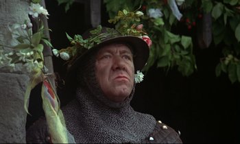 Movie still from “Monty Python and the Holy Grail” (1975), directed by Terry Gilliam – A man wearing a hat and a chain mail armor; Close Up shot, Low angle