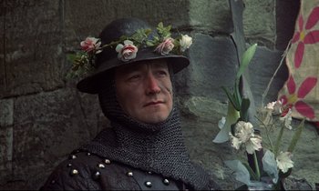 Movie still from “Monty Python and the Holy Grail” (1975), directed by Terry Gilliam – A man wearing a flower crown and a chain - mail outfit; Close Up shot, High angle