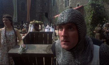 Movie still from “Monty Python and the Holy Grail” (1975), directed by Terry Gilliam – A man in a chain mail outfit and a crowd of people in the background; Close Up shot, Low angle