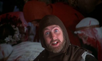 Movie still from “Monty Python and the Holy Grail” (1975), directed by Terry Gilliam – A person with a beard wearing a hood; Close Up shot, Over the shoulder angle