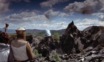 Movie still from “Monty Python and the Holy Grail” (1975), directed by Terry Gilliam – A man in a white hat looking out over a valley; Extreme Wide shot, High angle