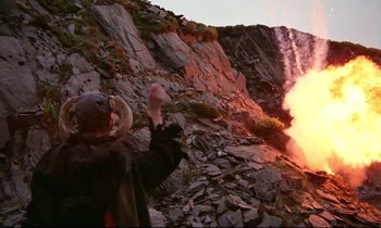 Movie still from “Monty Python and the Holy Grail” (1975), directed by Terry Gilliam – A person standing on top of a mountain near a fire; Wide shot, High angle