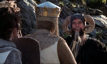 Movie still from “Monty Python and the Holy Grail” (1975), directed by Terry Gilliam – Two men dressed in medieval clothing and one is wearing a horned hat; Medium shot, Over the shoulder angle