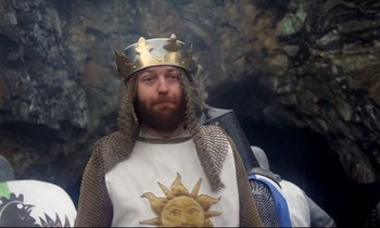 Movie still from “Monty Python and the Holy Grail” (1975), directed by Terry Gilliam – A man wearing a gold crown and a white and gold shirt; Medium shot, Low angle