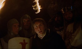 Movie still from “Monty Python and the Holy Grail” (1975), directed by Terry Gilliam – A group of people standing in a dark room; Close Up shot, Low angle
