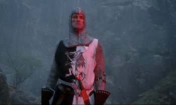 Movie still from “Monty Python and the Holy Grail” (1975), directed by Terry Gilliam – A man dressed as a medieval knight in chains; Medium shot, Low angle