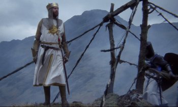 Movie still from “Monty Python and the Holy Grail” (1975), directed by Terry Gilliam – A man dressed as a king standing on top of a mountain; Wide shot, Low angle