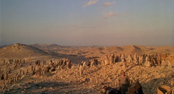 Movie still from “Life of Brian” (1979), directed by Terry Jones – A group of people sitting on top of a sandy beach; Extreme Wide shot, High angle