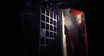 Movie still from “Life of Brian” (1979), directed by Terry Jones – A dark room with an open door to a cell; Wide shot, Low angle