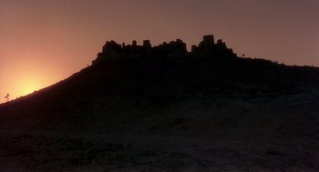 Movie still from “Life of Brian” (1979), directed by Terry Jones – The sun is setting over a hill with a castle like structure; Extreme Wide shot, Low angle