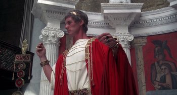 Movie still from “Life of Brian” (1979), directed by Terry Jones – A man dressed as a roman emperor standing in front of columns; Medium shot, Low angle