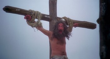 Movie still from “Life of Brian” (1979), directed by Terry Jones – A man hanging from a wooden cross with ropes around his neck; Medium shot, Low angle