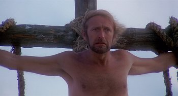Movie still from “Life of Brian” (1979), directed by Terry Jones – A shirtless man with a long blond hair hanging on a cross; Close Up shot, Low angle