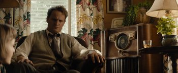 Movie still from “Mudbound” (2017), directed by Dee Rees – A man sitting in front of an old fashioned radio; Medium shot, Over the shoulder angle