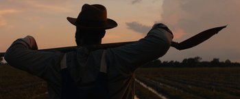 Movie still from “Mudbound” (2017), directed by Dee Rees – A man in a hat holding onto a pole in a field; Medium shot, Low angle