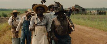Movie still from “Mudbound” (2017), directed by Dee Rees – A group of people walking down a dirt road; Medium shot, High angle
