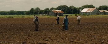 Movie still from “Mudbound” (2017), directed by Dee Rees – A group of people in a field with a barn in the background; Extreme Wide shot, High angle
