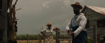 Movie still from “Mudbound” (2017), directed by Dee Rees – Two people standing next to a fence in a field; Medium shot, Low angle