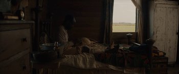 Movie still from “Mudbound” (2017), directed by Dee Rees – A man sitting on top of a bed next to a window; Wide shot, Over the shoulder angle
