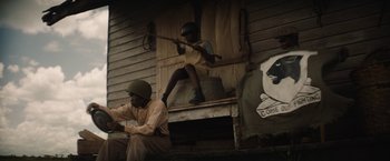 Movie still from “Mudbound” (2017), directed by Dee Rees – Two men sitting in front of a wooden building; Wide shot, Low angle