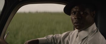 Movie still from “Mudbound” (2017), directed by Dee Rees – A man in a hat driving a car in a grassy field; Close Up shot, Over the shoulder angle