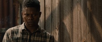 Movie still from “Mudbound” (2017), directed by Dee Rees – A man in a plaid shirt standing in front of a wooden wall; Close Up shot, Over the shoulder angle