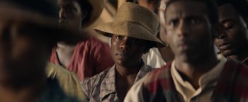 Movie still from “Mudbound” (2017), directed by Dee Rees – A man wearing a straw hat in a crowd of people; Close Up shot, Over the shoulder angle