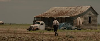 Movie still from “Mudbound” (2017), directed by Dee Rees – A man walking on a dirt road near an old farm house; Extreme Wide shot, Low angle