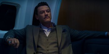 Movie still from “Murder Mystery” (2019), directed by Kyle Newacheck – A man in a suit and tie sitting down; Close Up shot, Low angle