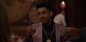 Movie still from “Murder Mystery” (2019), directed by Kyle Newacheck – A man wearing a suit and gold jewelry; Close Up shot, Over the shoulder angle