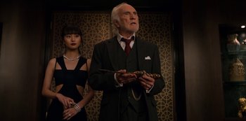 Movie still from “Murder Mystery” (2019), directed by Kyle Newacheck – An older man in a suit and tie holding a cane; Medium shot, Low angle