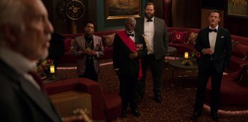 Movie still from “Murder Mystery” (2019), directed by Kyle Newacheck – A group of men standing next to each other in a room; Wide shot, Over the shoulder angle