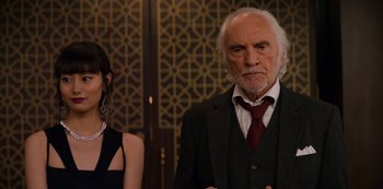 Movie still from “Murder Mystery” (2019), directed by Kyle Newacheck – An older man and a young woman standing next to each other; Close Up shot, Over the shoulder angle