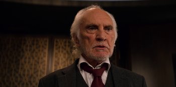 Movie still from “Murder Mystery” (2019), directed by Kyle Newacheck – An older man wearing a suit and a red neck tie; Close Up shot, Low angle