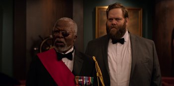 Movie still from “Murder Mystery” (2019), directed by Kyle Newacheck – A man in a suit and tie standing next to another man in a suit and tie; Medium shot, Low angle