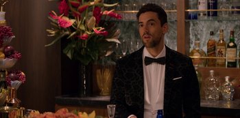 Movie still from “Murder Mystery” (2019), directed by Kyle Newacheck – A man in a tuxedo sitting in front of a flower arrangement; Close Up shot, Over the shoulder angle