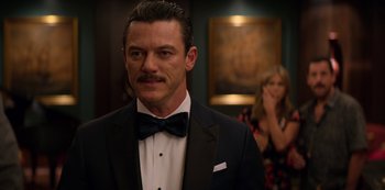 Movie still from “Murder Mystery” (2019), directed by Kyle Newacheck – A man in a suit and a bow tie; Close Up shot, Over the shoulder angle