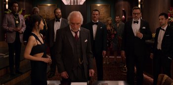 Movie still from “Murder Mystery” (2019), directed by Kyle Newacheck – A group of people in suits and ties in a room; Wide shot, Over the shoulder angle