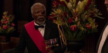 Movie still from “Murder Mystery” (2019), directed by Kyle Newacheck – An older man in a tuxedo holding medals; Medium shot, Over the shoulder angle