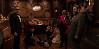 Movie still from “Murder Mystery” (2019), directed by Kyle Newacheck – A group of people sitting on the floor of a room; Wide shot, High angle