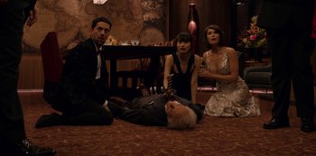 Movie still from “Murder Mystery” (2019), directed by Kyle Newacheck – A group of people sitting on the floor next to a man; Medium shot, High angle