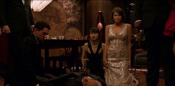 Movie still from “Murder Mystery” (2019), directed by Kyle Newacheck – Two women and a man are standing in front of a table; Medium shot, High angle