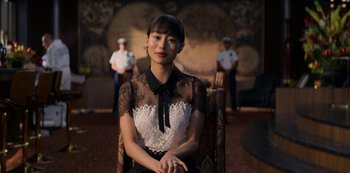 Movie still from “Murder Mystery” (2019), directed by Kyle Newacheck – A woman sitting in a chair in front of two other people; Close Up shot, Over the shoulder angle