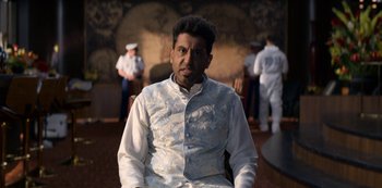 Movie still from “Murder Mystery” (2019), directed by Kyle Newacheck – A man sitting in front of a group of people; Close Up shot, Low angle