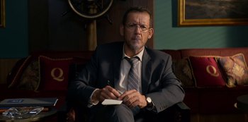 Movie still from “Murder Mystery” (2019), directed by Kyle Newacheck – A man in a suit and tie writing on a piece of paper; Medium shot, Low angle