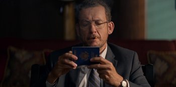Movie still from “Murder Mystery” (2019), directed by Kyle Newacheck – A man in a suit smoking a cigarette while looking at a passport; Close Up shot, Low angle