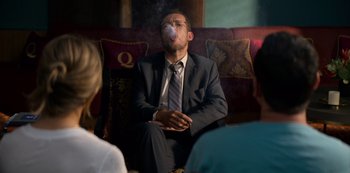 Movie still from “Murder Mystery” (2019), directed by Kyle Newacheck – A man sitting on a couch smoking a cigarette; Medium shot, Over the shoulder angle