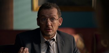 Movie still from “Murder Mystery” (2019), directed by Kyle Newacheck – A person wearing a suit and glasses; Close Up shot, Over the shoulder angle