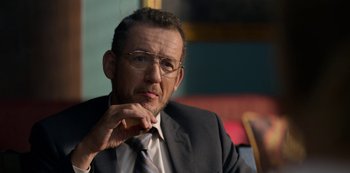 Movie still from “Murder Mystery” (2019), directed by Kyle Newacheck – A man in a suit and tie sitting in front of a window; Close Up shot, Over the shoulder angle