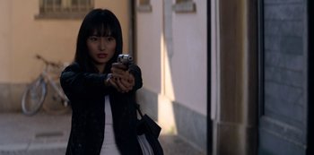 Movie still from “Murder Mystery” (2019), directed by Kyle Newacheck – A woman holding a gun in her hand; Medium shot, Over the shoulder angle